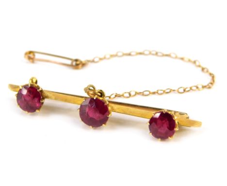 A bar brooch, set with three dark red stones, each in claw setting, on a single pin back with safety chain, yellow metal unma