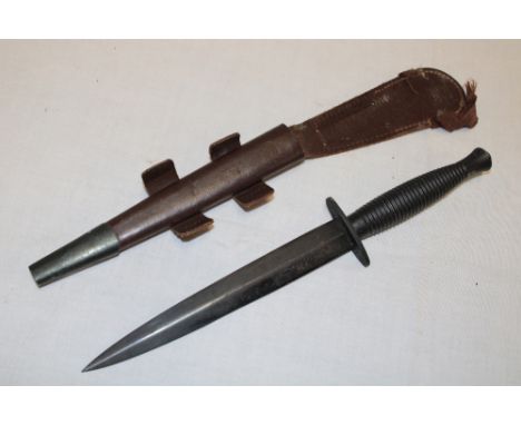 A post-War Commando dagger with 7" blade by Wilkinson Sword, blackened ribbed hilt in leather sheath