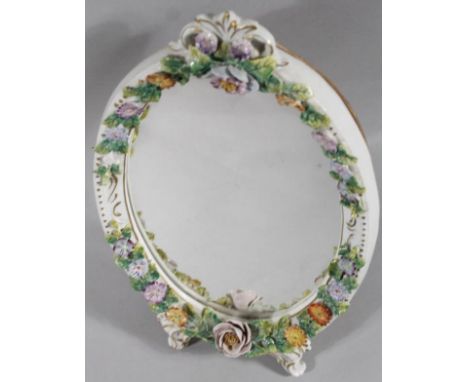 A 20thC Sitzendorf table mirror, the oval glass decorated with a flower head border, on gilt highlighted scroll feet, with a 