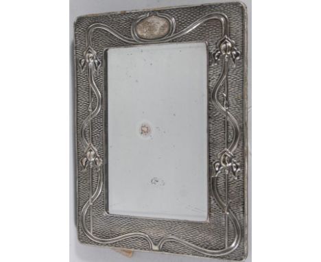 An Edwardian Art Nouveau silver mirror, of rounded rectangular outline, raised with lotus flowers, stems and flower heads, wi