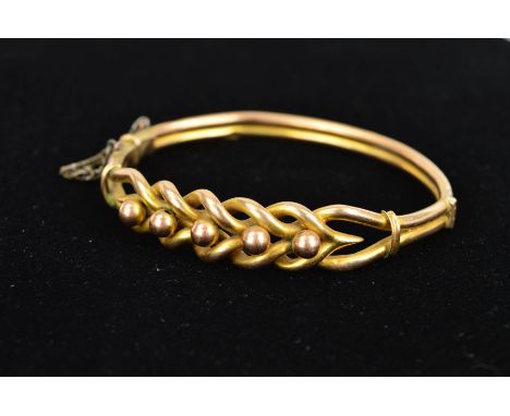 AN EARLY 20TH CENTURY 9CT GOLD HINGED BANGLE, the front an openwork interwoven design with bead detail tapering to the double