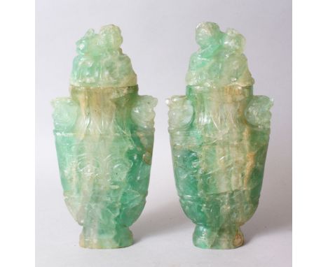 A GOOD PAIR OF CHINESE CARVED JADE LIDDED URNS, carved in archaic style with scrolling foliage amongst lion dogs 23.5cm high 
