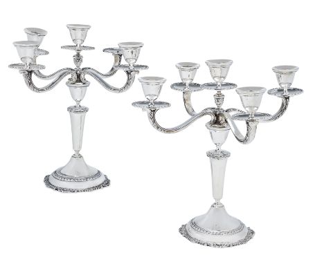 A pair of silver plated five light candelabra. The tapering stems to circular feet designed with foliate scroll and shell bor