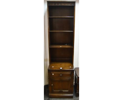 A slender Ercol shelving unit of four shelves projecting base enclosing single drawer above cross banded panelled door