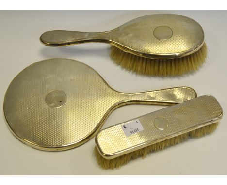 A silver backed three piece dressing table set, comprising hair brush, hand mirror and clothes brush, engine turned back