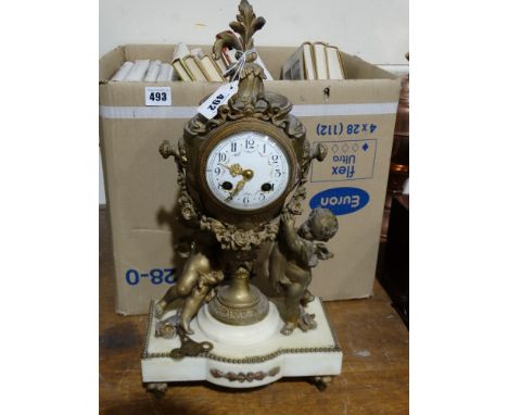 A Gilt Spelter & White Marble Based, Mantel Clock With Circular White Enamel Dial, Modelled As An Urn With Cherubs At Feet