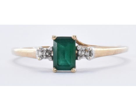 A hallmarked 9ct gold ring set with an emerald cut synthetic emerald flanked by two diamond accent stones. Assay marked Birmi