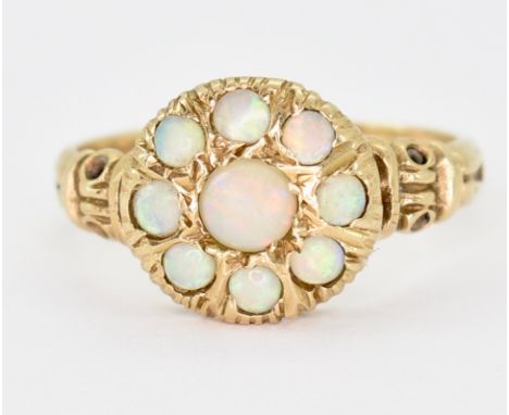 A hallmarked 9ct gold and opal cluster ring. The ring set with 9 opal cabochons mounted within a circular head to scrolled de