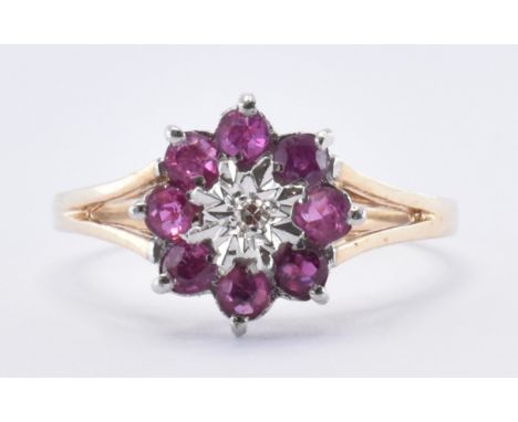 A 9ct gold ruby and diamond cluster ring. The ring having a a central round cut diamond within an illusion setting surrounded