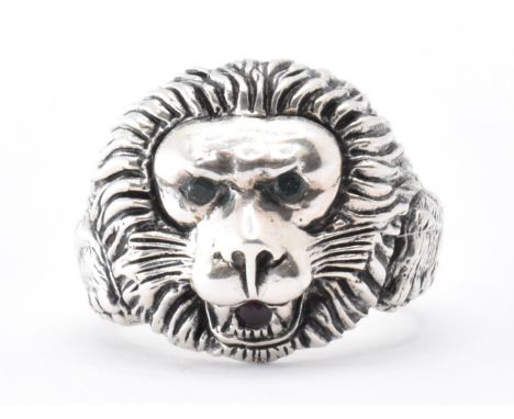 A silver lion mask ring. The ring having a moulded lion to the head being set with green stone eyes and a red stone to the mo