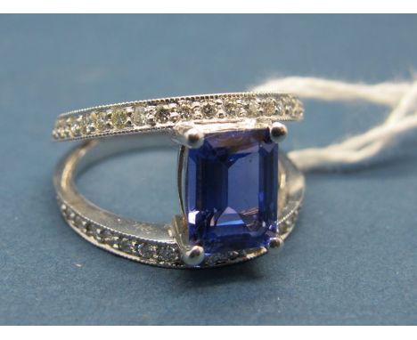 A Modern 18ct White Gold Tanzanite and Diamond Set Dress Ring, the central emerald cut tanzanite claw set between two bands o