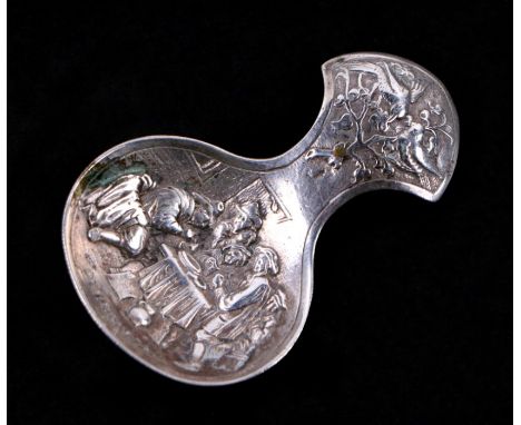 A 19th century Dutch white metal caddy spoon with repousse decoration depicting figures around a table, 16g.