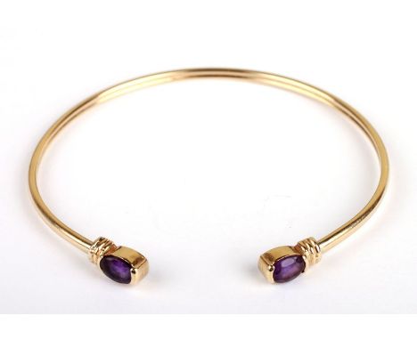 A gold (unmarked but tested for 9ct) bangle with amethyst set ends, 7cms diameter, 6.9g.