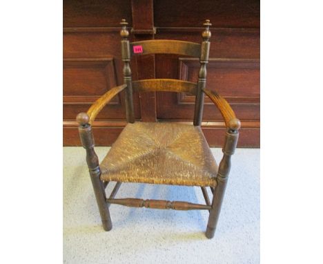 An early 20th century child's oak framed, ladder back open arm chair with rush seat