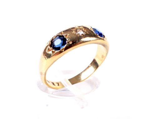 An early 20th century gold, sapphire and diamond three stone gypsy ring. Centred with a small old-cut diamond between round m