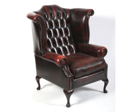 A Georgian style button back wing armchair. Upholstered in dark red studded leatherette, with drop-in cushion, on cabriole fe