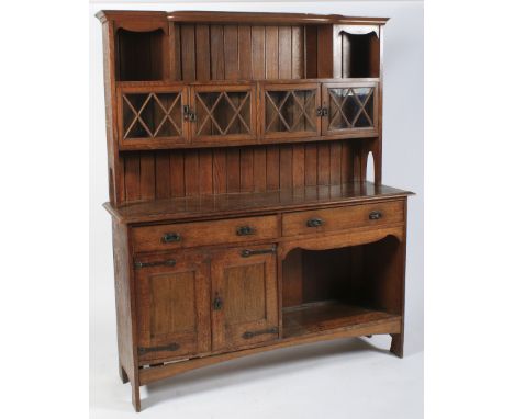 An Arts and Crafts Liberty style oak dresser, circa 1900. The moulded shaped cornice above three open shelves and four glazed