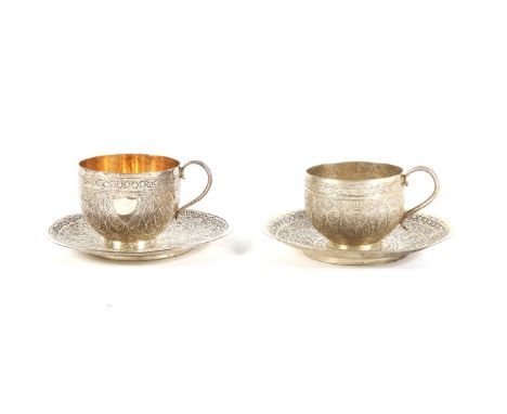 Two Middle Eastern white metal teacups and saucers. Each cast with dense interlocking scrolls and flowering branches and flow
