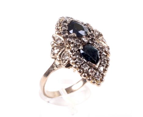 A dark-blue sapphire and diamond dress ring in the form of a stylised shoe buckle. With two pear-shaped sapphires within eigh