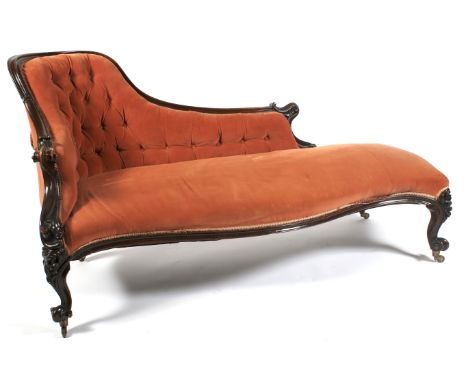 A Victorian mahogany framed button back chaise longue. Of scroll form carved with foliate scroll moulded frame, upholstered i