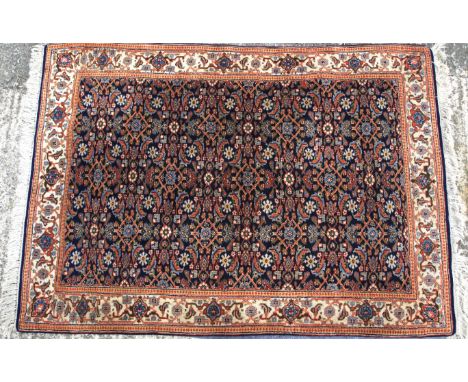 A 20th century rug. The central panel featuring flowers and foliage on a blue ground, with a cream border, tassels to either 