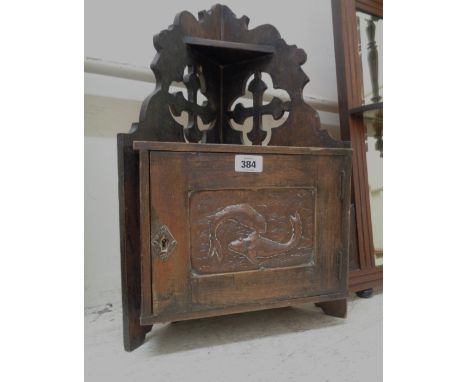 A small old oak corner shelf with pierced Gothic cross decoration to top, over a single cupboard door inset with an embossed 