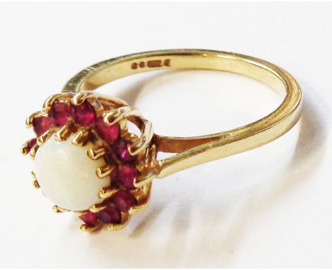 A 375 (9ct.) gold ring, set with central cabochon opal within a dark ruby encrusted border - size N 1/2 - boxed