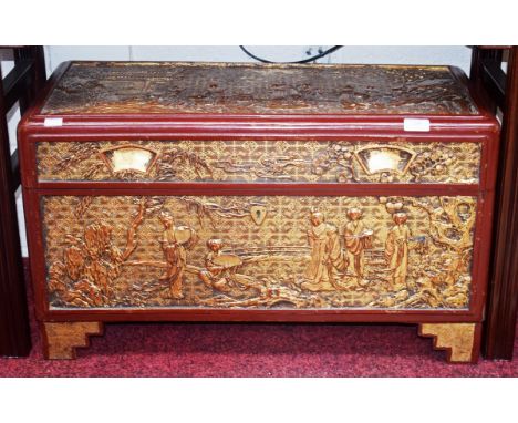 A CHINESE CARVED AND RED LACQUERED CAMPHORWOOD CHEST, O.R.M., the top with figures and pagodas in relief, and conforming fron