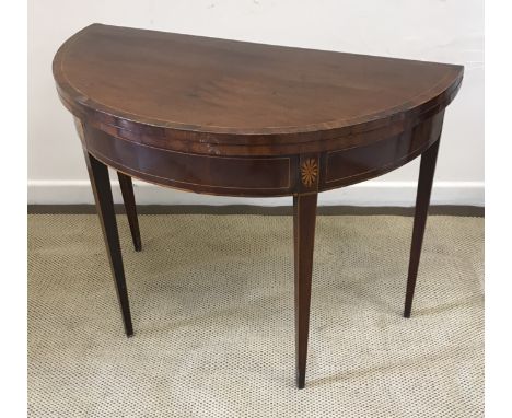 A late George III mahogany and inlaid fold-over card table of demi-lune form, the cross-banded top opening to reveal a green 