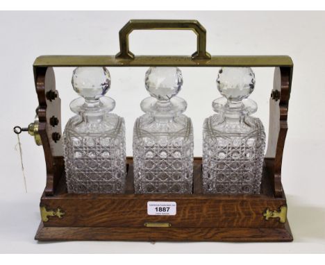 Early 20th Century oak and brass mounted three bottle tantalus marked Betjemann's patent, London, 23195, with three hobnail c