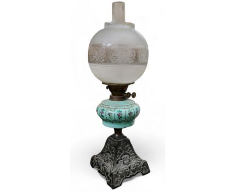 An early 20th century oil lamp, cast ebonised metal base with winged cherub mask details, painted glass reservoir, etched gla