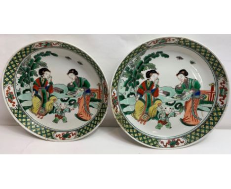 A pair of Chinese plates, each decorated with two seated females and a boy playing, 24.5cm diameter