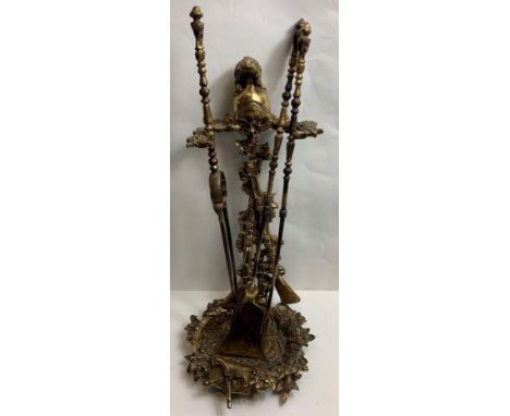 A brass fire iron stand, with shotgun decoration back with a helmet finial