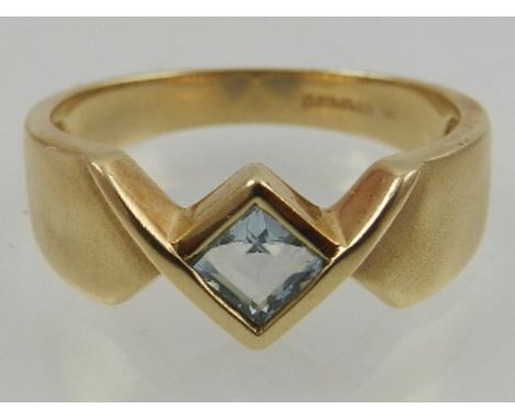 A 9 carat yellow gold and aquamarine ring, set square cut stone within a brushed crossover mount. 