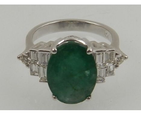 An 18 carat white gold, diamond, and emerald ring, the oval cut emerald 0f 4.50 carats, flanked by eight graduated baguette c