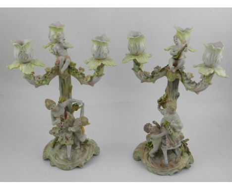 A pair of a German three branch porcelain candelabra, encrusted with flowers, having cherub playing the mandolin to top, the 