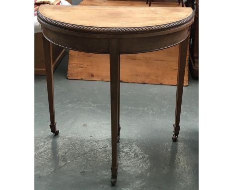 A faded mahogany demilune card table, fold-over top on square tapered legs, with spayed feet and casters, 76cmD 