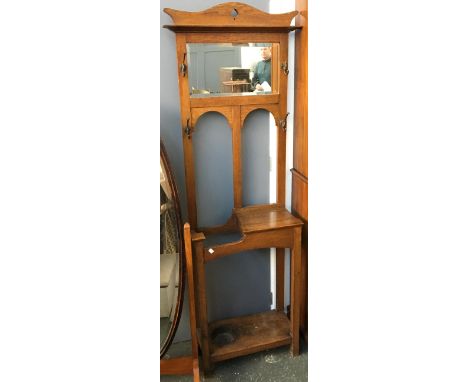 An oak coat and stick stand, having bevelled glass mirror and coat hooks, hinged lidded compartment and drip tray, 56x182cmH 