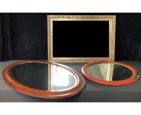 An Edwardian mahogany inlaid oval bevelled glass mirror; a Chinese red lacquered oval bevelled glass mirror; a gilt oblong mi