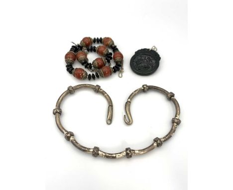 A Chinese black stone carved pendant 40mm wide, a silver necklace and one other necklace.