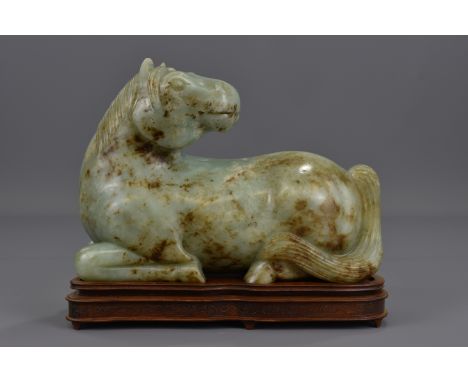 A Chinese Ming Dynasty or later celadon jade carving of a horse on a hardwood stand. 25cm tall