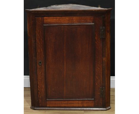 A George III oak splay fronted wall hanging corner cupboard, moulded cornice above a rectangular panel door enclosing three s