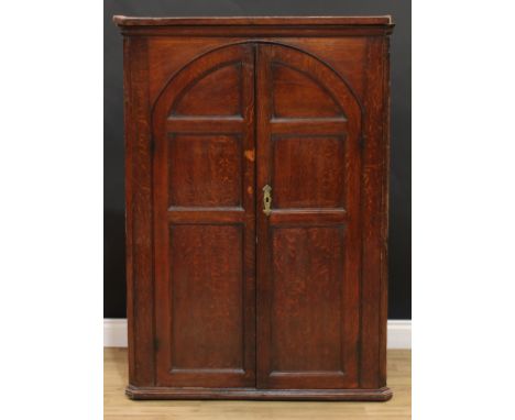 A large George III oak wall hanging corner cupboard, moulded cornice above a pair of arched panel doors enclosing three shape