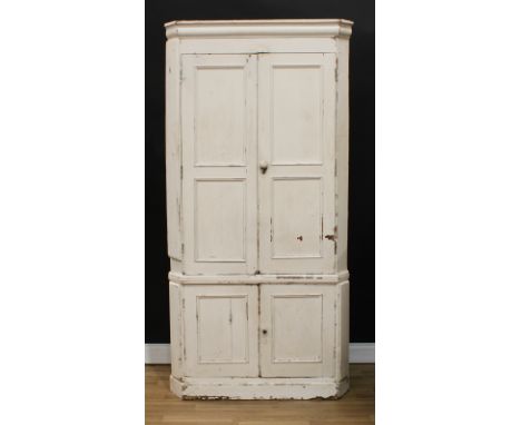 A 19th century painted pine country house floor-standing corner cupboard, moulded cornice above two pairs of panel doors, the