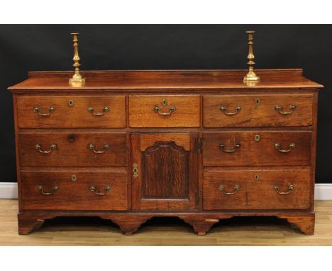 An 18th century oak low dresser, rectangular top above an arrangement of five drawers and an arched panel door, brass swan ne