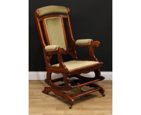 A late 19th century American spring rocking chair, stuffed-over upholstery, scroll hand rests, shaped apron, ceramic fore cas