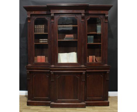 A Victorian mahogany break-centre library bookcase, outswept cornice above three glazed doors, each enclosing two adjustable 