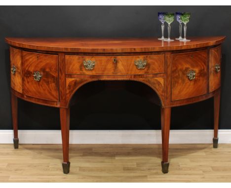 A George III mahogany demilune sideboard or serving table, slightly oversailing top centred by a shell patera, above a centra