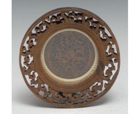 A Chinese sandalwood roundel, carved in relief with traditional figures, blossom, and garden architecture, the outswept borde