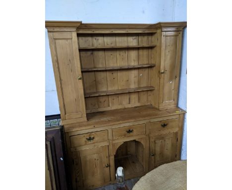 A panelled pine dresser, late 19th/early 20th century, stepped cornice above three open shelves with display hooks, flanked b